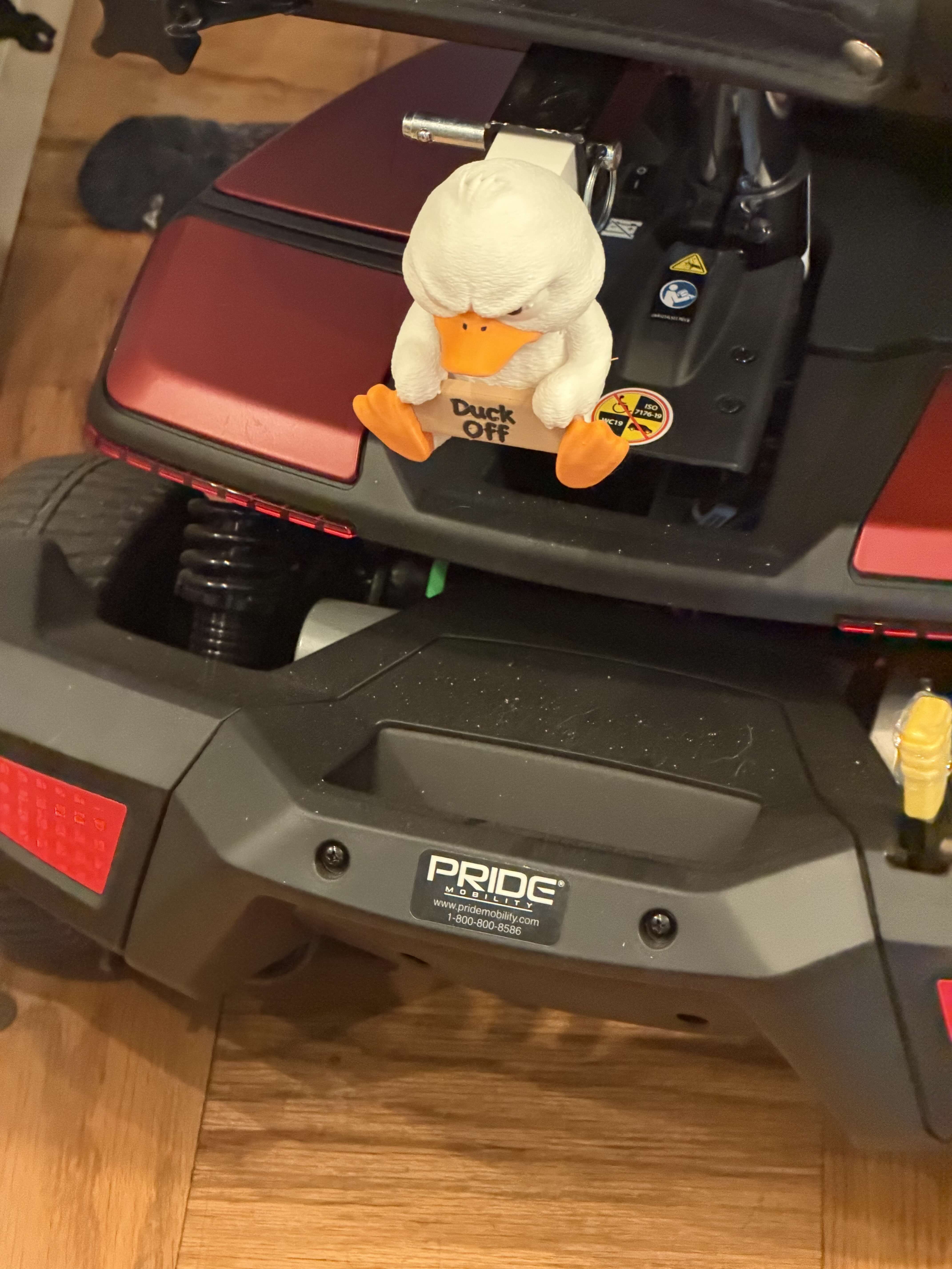 The Duck Off ornament mounted on the rear rack of a mobility scooter, seen from behind